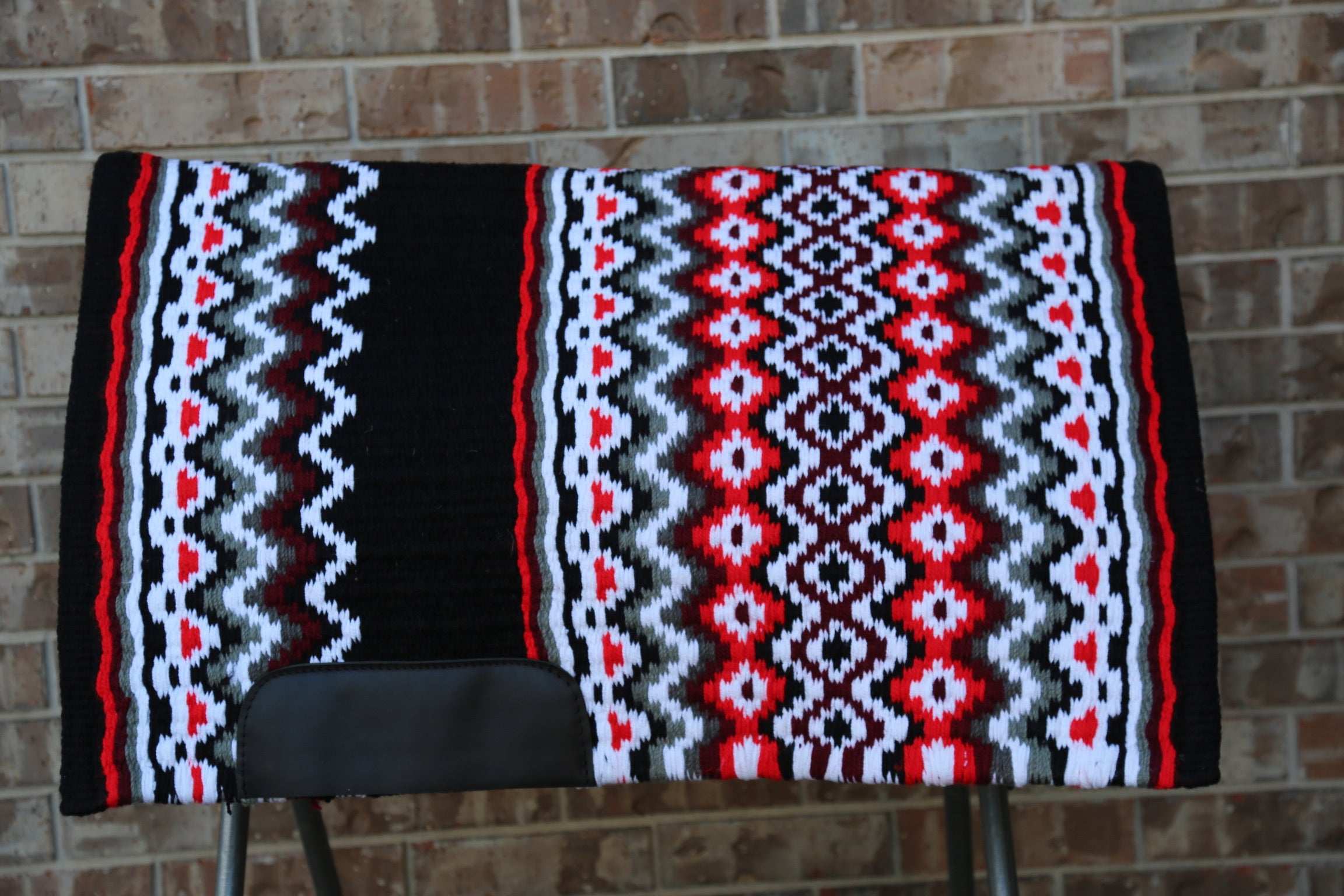 Custom Western Saddle Pad in Red, Brown, White, Black geometric color pattern| Limited Edition displayed on saddle rack with brick background