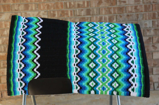 Custom Western Saddle Pad in Blue, Green, White, Black geometric color pattern displayed on a saddle rack with brick background | Limited Edition