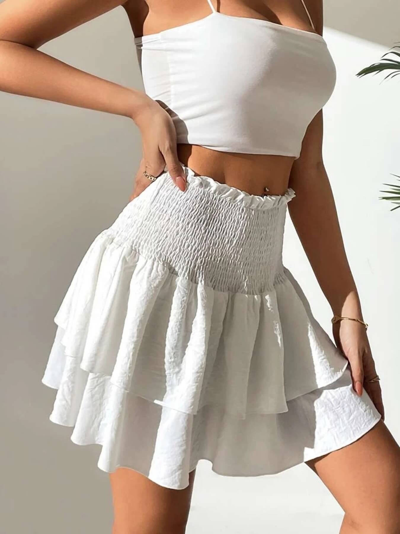 Person wearing a white crop top and smoked layered mini skirt against a neutral background