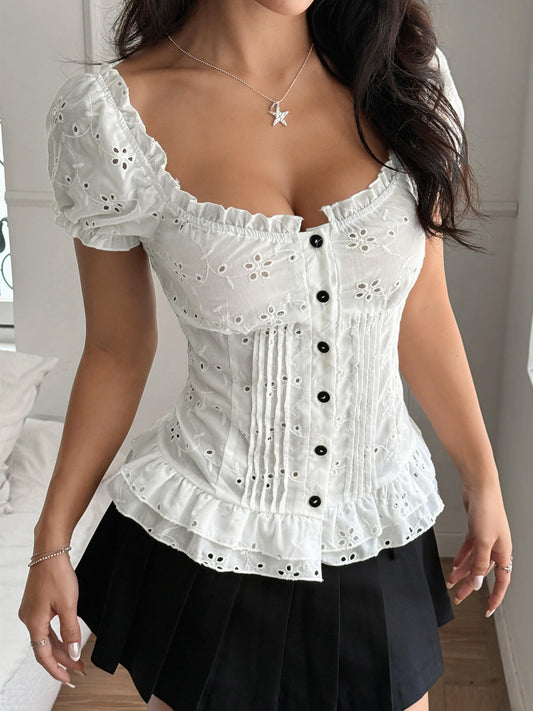 Woman wearing a white lace top with black buttons and a black skirt indoors.