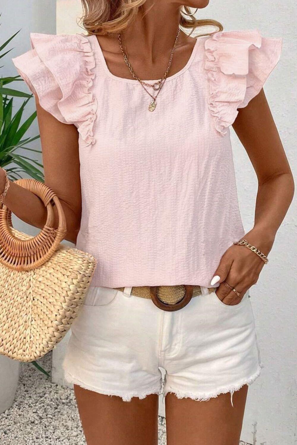 Woman wearing a pink ruffled top and white shorts, holding a straw bag.