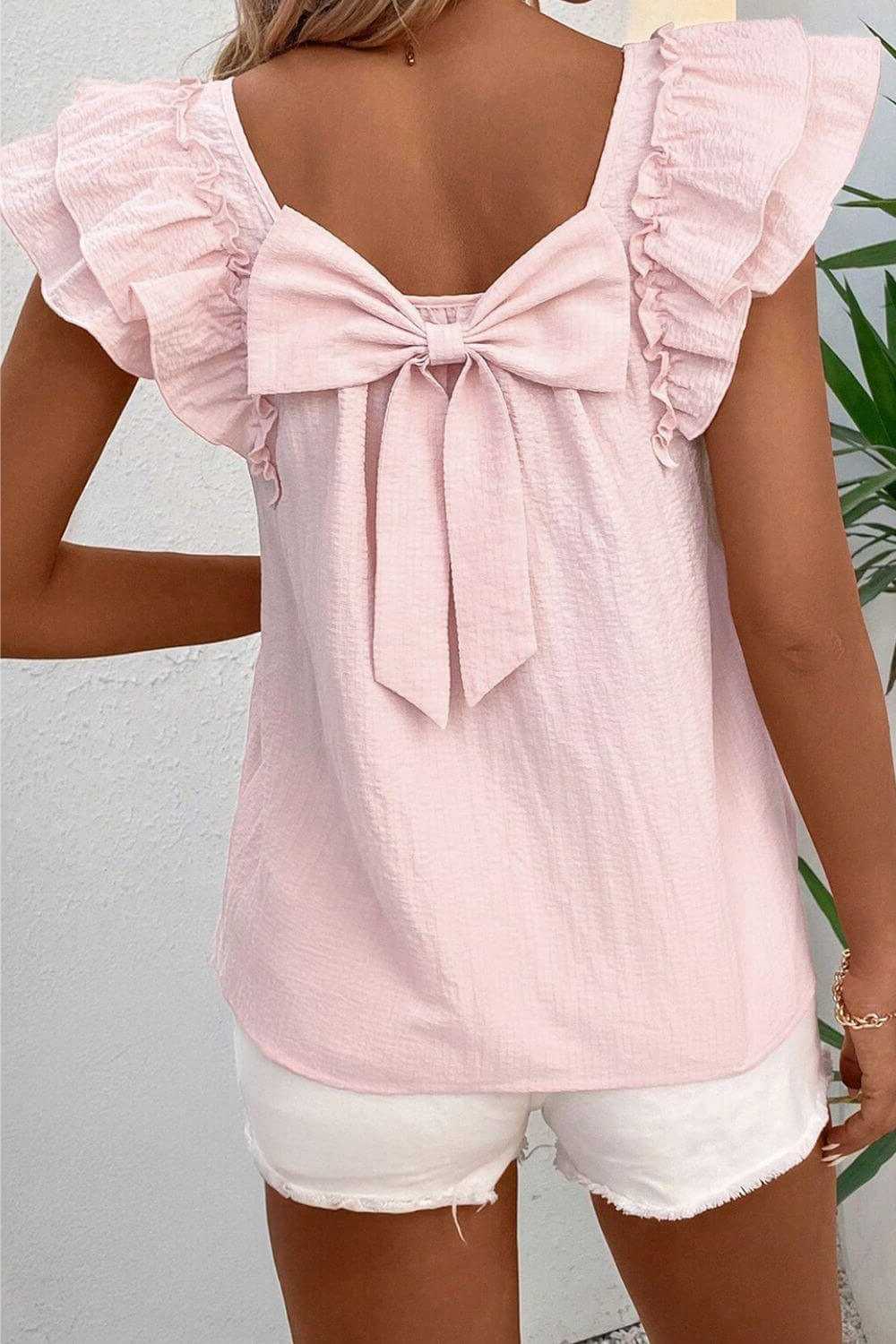 Pink ruffled top with a bow detail worn by a woman, against a neutral background.