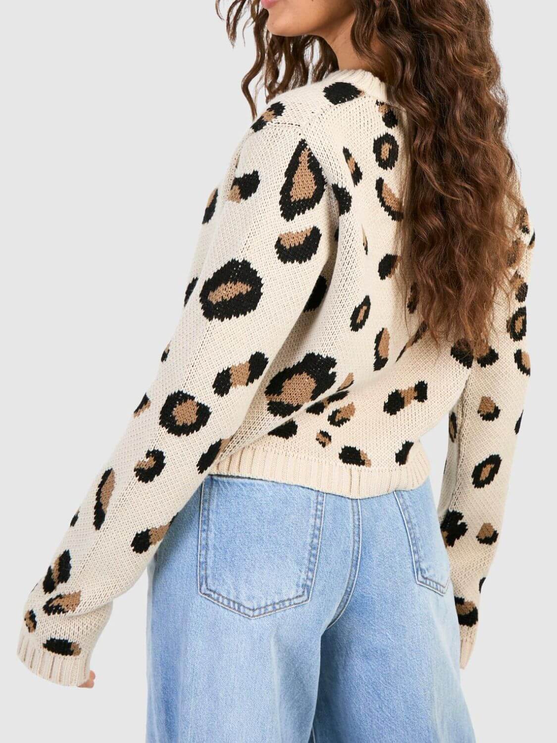 Woman wearing a cream sweater with leopard print pattern and light blue jeans on a white background
