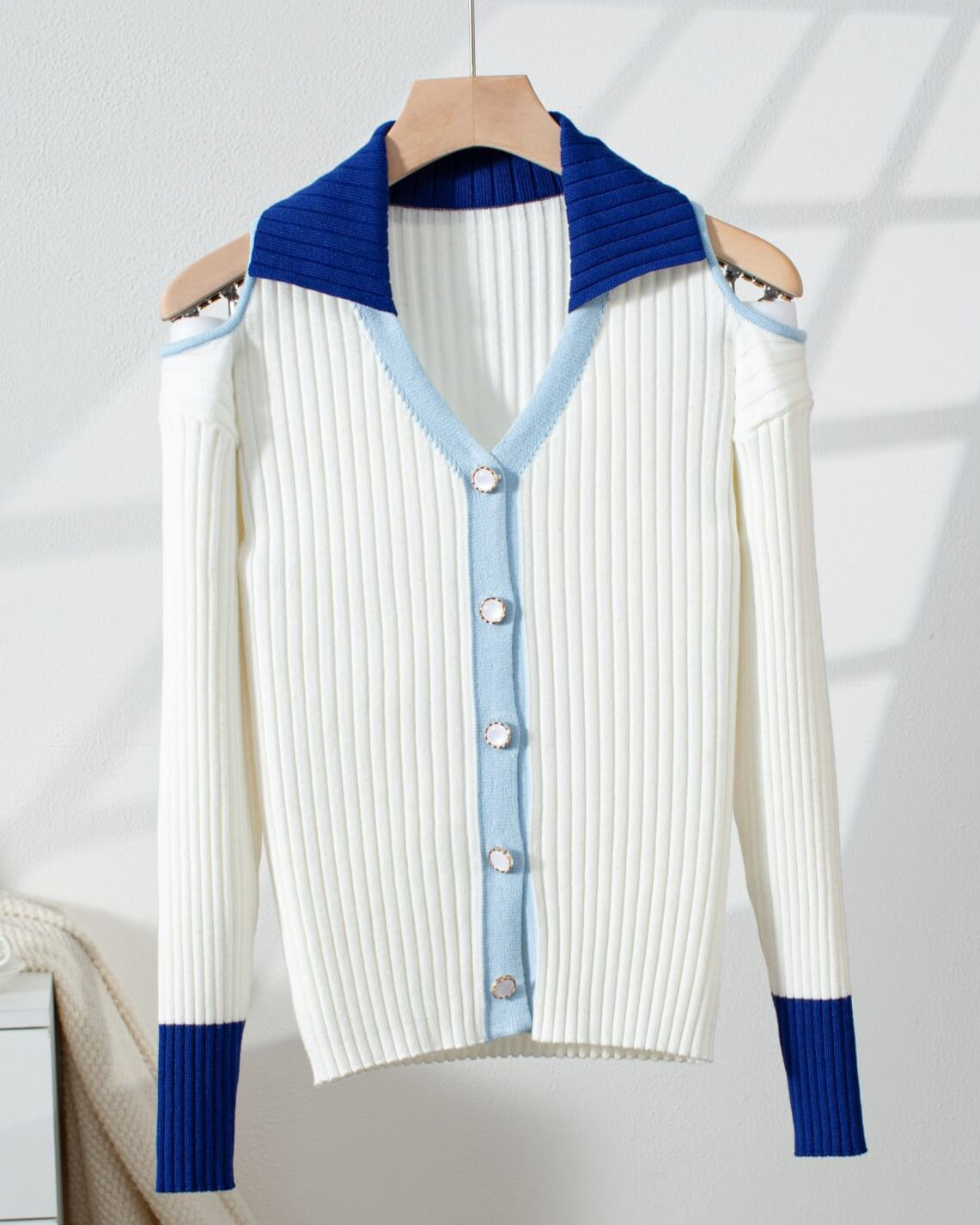 White cold shoulder cardigan sweater with blue and light blue accents on a hanger against a white background