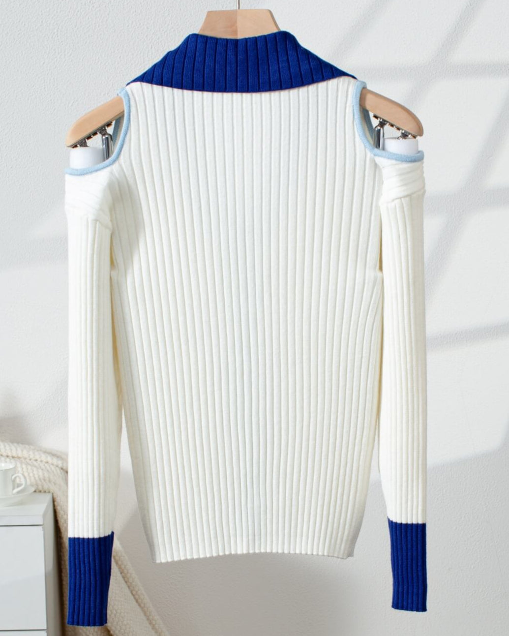 Back of White cold shoulder cardigan sweater with blue and light blue accents on a hanger against a white background