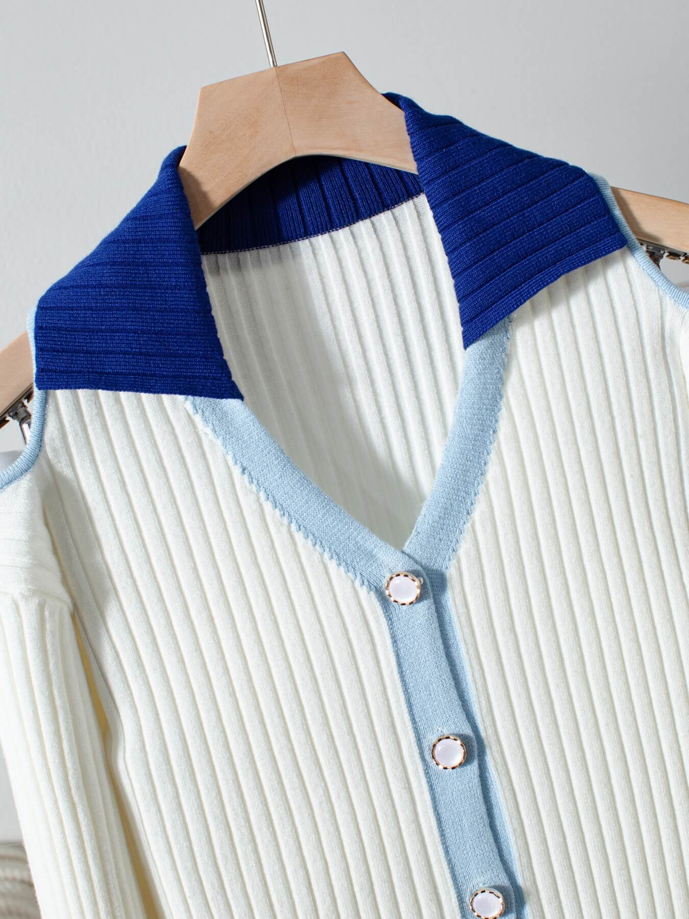 White cold shoulder cardigan with blue collar and trim on a hanger against a light gray background
