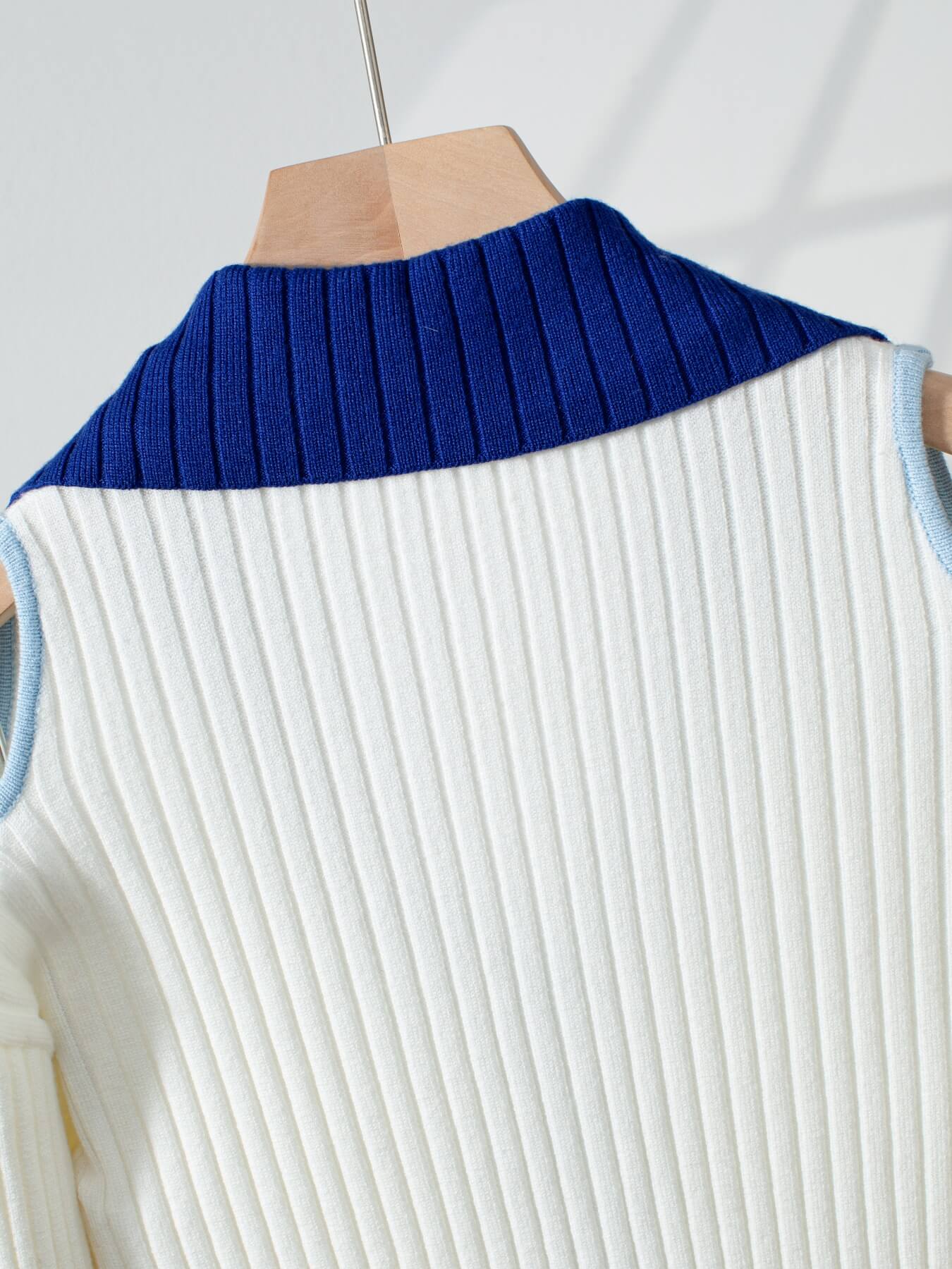 White ribbed cold shoulder sweater with blue collar on a wooden hanger against a light gray background