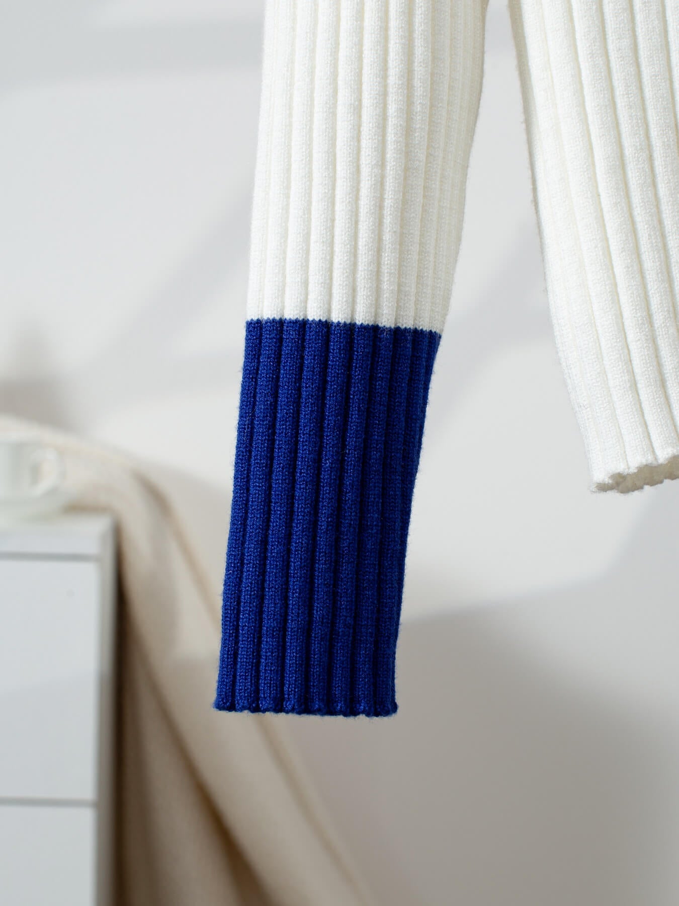 Close-up of a white sweater with a blue sleeve against a blurred background