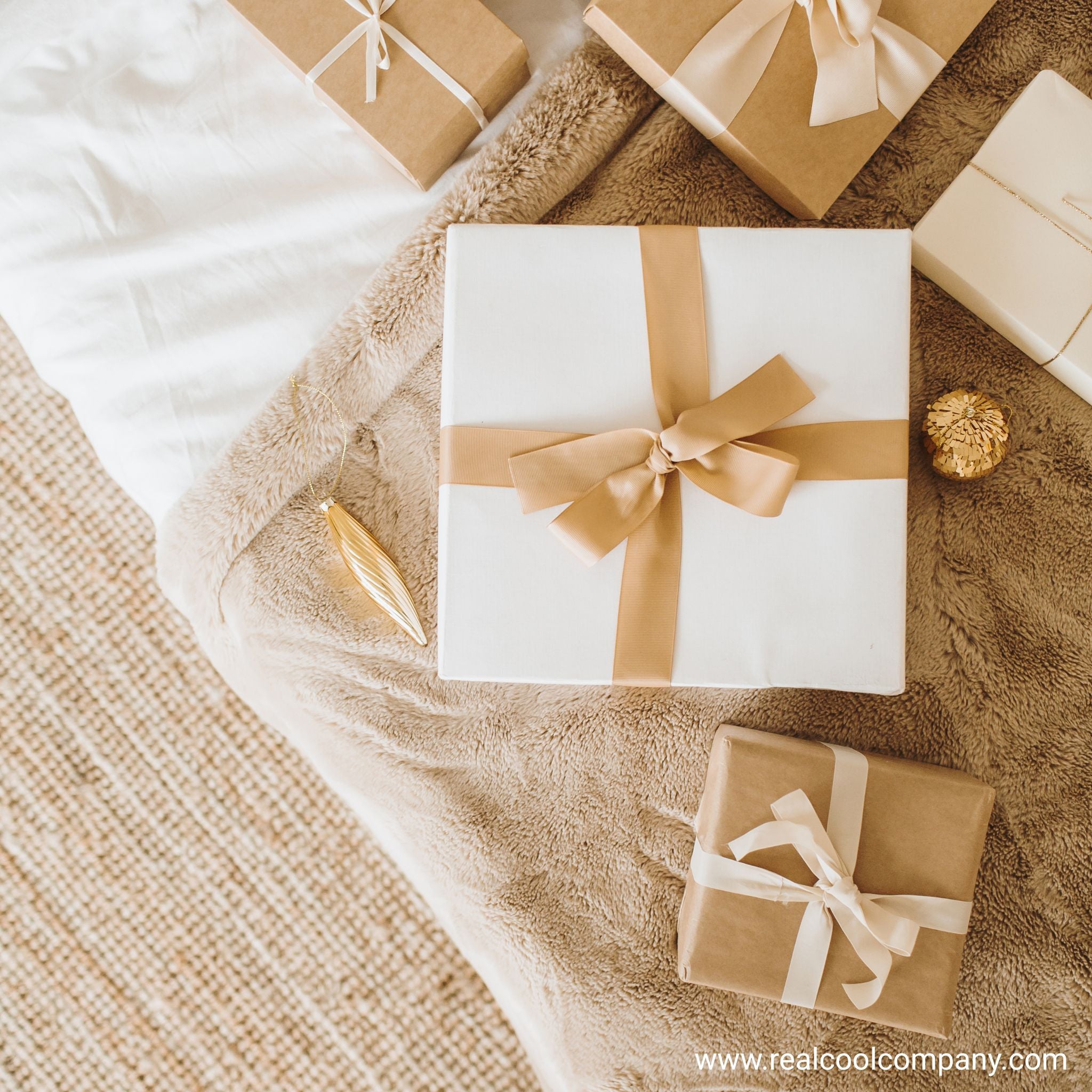 Gift boxes with ribbons on a textured surface, featuring the Real Col Company logo.